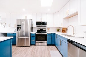 Una cocina moderna con electrodomésticos de acero inoxidable, armarios azules y encimera blanca.