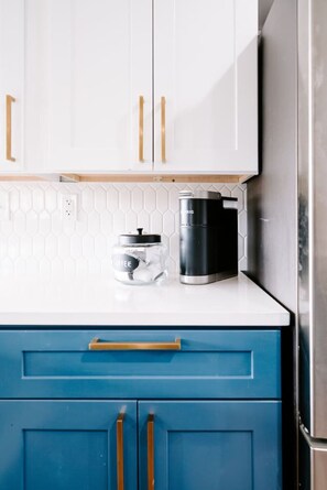 Una cocina con armarios blancos, una cafetera y un tarro de café.