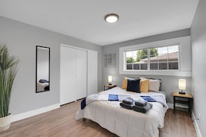 A bedroom with a bed, bedside tables, a window, a mirror, and a potted plant.