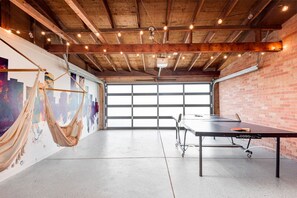 A spacious room with a ping pong table, a hammock, and a cityscape mural on the wall.