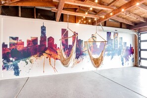Een ruime garage met een stadsgezichtsmural op de muur, twee hangmatten en zichtbare houten balken.