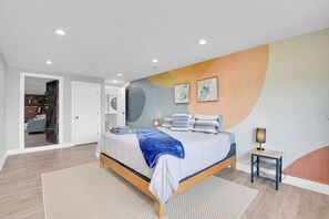 Ein modernes Schlafzimmer mit Bett, Nachttisch und einer Wand mit abstrakter Kunst.