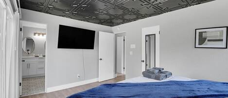 A bedroom with a bed, a TV, a door, and a bathroom visible in the background.