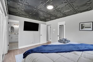A bedroom with a bed, a TV, a door, and a bathroom visible in the background.