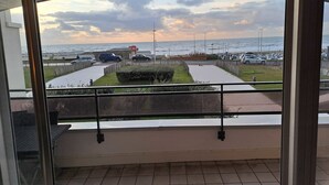 Vista desde un balcón sobre un paseo marítimo con coches estacionados, una valla y un cartel del hotel 'Ibis'.