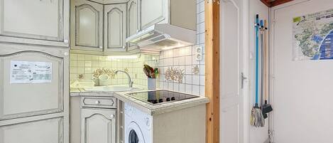 A compact kitchen with a built-in washing machine, a small sink, and a tiled backsplash.