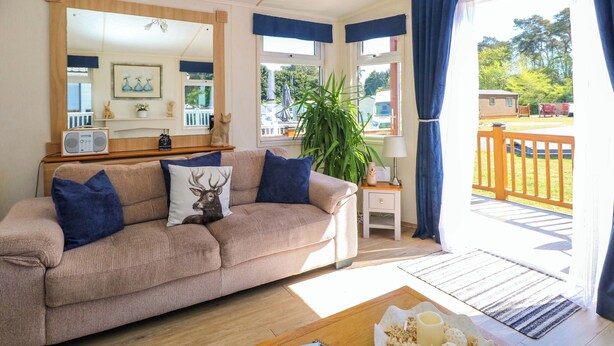 A cozy living room with a sofa, a mirror, a radio, a plant, and a view of the outdoors. - 25 Foxburrow Hang (Great Yarmouth)