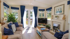 A living room with a sofa, television, fireplace, and a view through a glass door. - 25 Foxburrow Hang (Great Yarmouth)