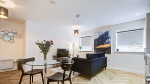 A modern living room with a glass coffee table, dark sofas, and a flat-screen TV. - Hybrid Resi - Mitcham  (Mitcham)