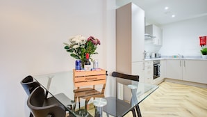 A modern kitchen with white cabinets, a wooden table with a 'Welcome' sign, and a glass dining table with chairs. - Hybrid Resi - Mitcham  (Mitcham)