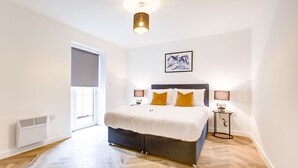 A bedroom with a bed, bedside lamps, a radiator, a window with blinds, and a ceiling light fixture. - Hybrid Resi - Mitcham  (Mitcham)