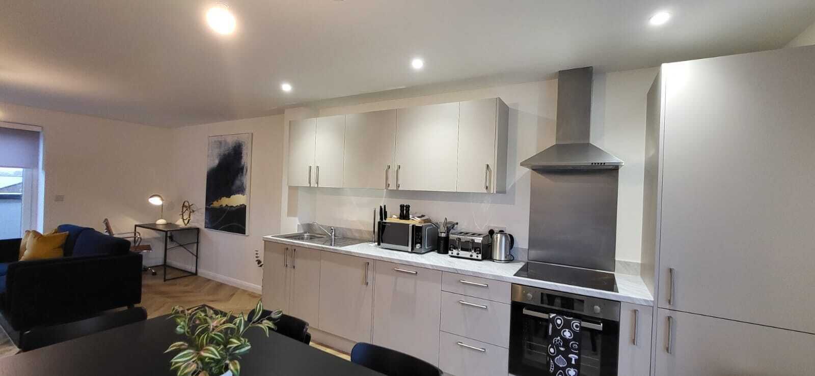 Una cocina moderna con armarios blancos, una campana extractora de acero inoxidable y un comedor con mesa y sillas.