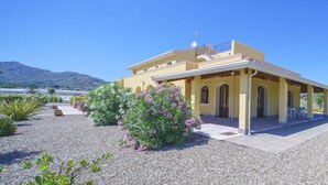 A yellow building with a covered patio, surrounded by gravel and flowering plants. - MINISSALE FARMHOUSE (Calatabiano)