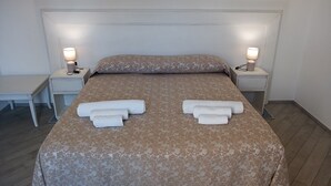 A neatly made bed with a floral-patterned bedspread, two bedside tables with lamps, and a small desk with a chair. - MINISSALE FARMHOUSE (Calatabiano)