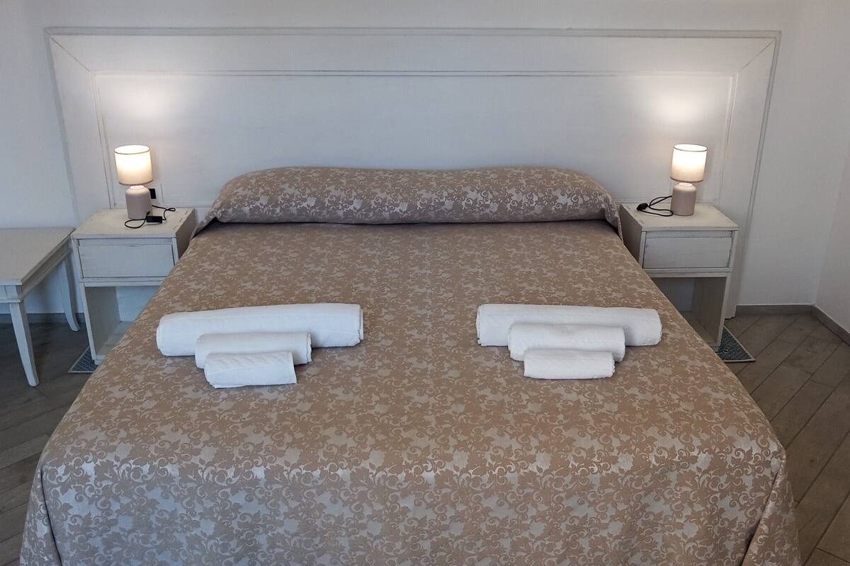 A neatly made bed with a floral-patterned bedspread, two bedside tables with lamps, and a small desk with a chair.