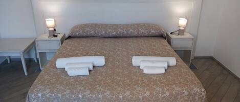 Una cama bien hecha con una colcha de estampado floral, dos mesitas de noche con lámparas y un pequeño escritorio con una silla.