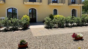 A two-story building with a yellow facade, multiple balconies, and a gravel courtyard with potted plants. - MINISSALE FARMHOUSE (Calatabiano)