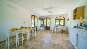 A spacious dining area with a wooden table set for a meal, surrounded by white chairs. - MINISSALE FARMHOUSE (Calatabiano)