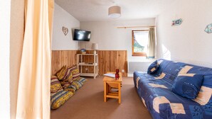 Une pièce chaleureuse avec un canapé bleu, une table en bois et un téléviseur fixé au mur.