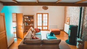 A cozy living room with a sofa, a bookshelf, a fireplace, and a window with wooden shutters. - Le Moulin de L'Isle - Maison chaleureuse (L'Isle-Bouzon)