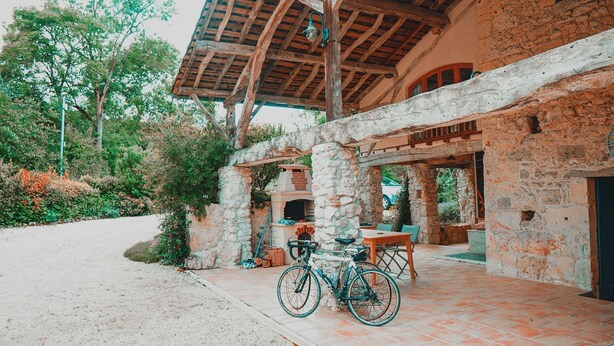 A stone building with a tiled patio, a bicycle, and outdoor seating. - Le Moulin de L'Isle - Maison chaleureuse (L'Isle-Bouzon)