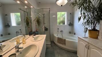 Une salle de bain moderne avec deux lavabos, une baignoire et une douche. On y trouve également des plantes en pot et un miroir.