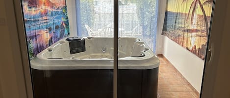 A spa tub with a control panel, a window with a view of a beach, and a tropical mural on the wall.