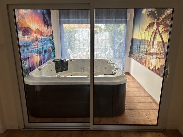 A spa tub with a control panel, a window with a view of a beach, and a tropical mural on the wall.