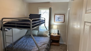 A bunk bed room with a window, a bedside table with a lamp, and a framed picture on the wall.