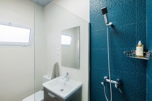 A bathroom with a white sink, a mirror, a window, and a shower with a blue textured wall. - Casa da Náu (Ponta Delgada)