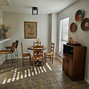 A dining area with a round table, four chairs, a potted plant, and a wall-mounted light fixture.