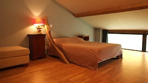 Une chambre avec un plafond en pente, un lit, une table de chevet, une lampe et une fenêtre.