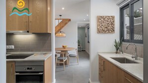A modern kitchen with wooden cabinets, a built-in oven, and a dining area with a round table and chairs. - Calheta beautiful character cottage | Villa Loreto (Arco Da Calheta)