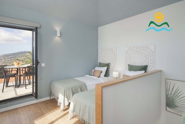 A bedroom with two beds, a balcony with a table and chairs, and a city view.