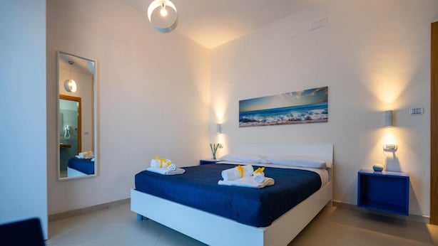 A modern hotel room with a large bed, a painting of a beach scene, and a mirror. - B & SunSea (Agropoli)