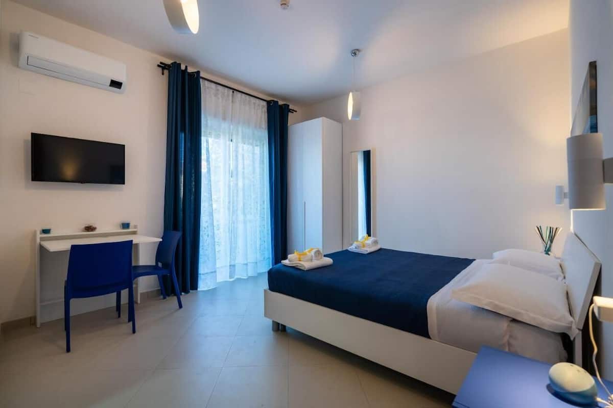 A hotel room with a bed, a desk, a chair, a TV, and a window with curtains.