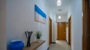 A hallway with a wooden shelf, a blue vase, a potted plant, and a painting on the wall. - B & SunSea (Agropoli)