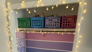Ein gemütliches Zimmer mit farbenfroher Wand, einem kleinen Bett mit blauer Decke und Regalkisten an der Wand.