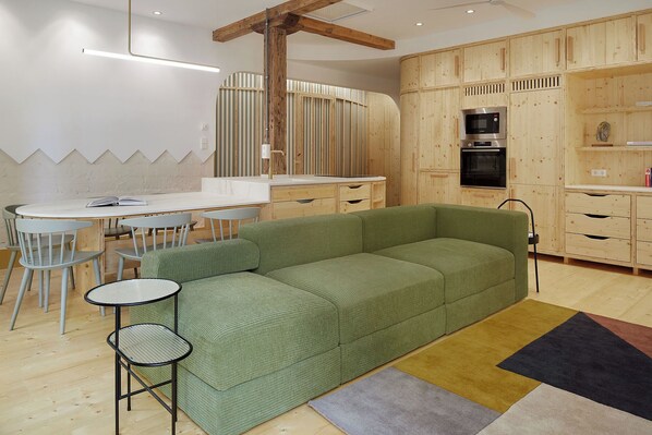 A modern kitchen with wooden cabinets, a green sofa, and a dining area with chairs and a table.