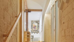 Un escalier en bois mène à une pièce dont un des murs est en pierre et qui est décorée d’une œuvre d’art aux couleurs vives.