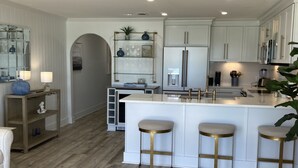 A modern kitchen with white cabinetry, a central island with stools, and a wooden floor. - SPECTACULAR FIRST FLOOR “BEACHFRONT”
CONDO COMPLETELY RENOVATED ON CRYSTAL BEACH (Destin)