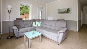 A modern living room with a grey sectional sofa, a glass coffee table, and a floor lamp. - Amselresidenz 2 - DROSSEL (Binz)