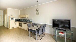 A modern kitchen with a dining table and chairs, a TV on a glass stand, and a microwave. - Amselresidenz 2 - DROSSEL (Binz)