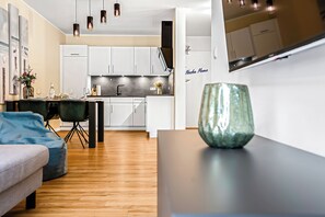 Une cuisine moderne avec des meubles blancs, un coin repas comprenant une table et des chaises, et un salon avec un canapé et un vase décoratif.