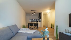 A modern living room with a grey sofa, a wooden coffee table with vases, and a kitchen in the background.