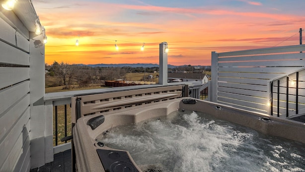 A hot tub with a view of a sunset over a rural landscape.