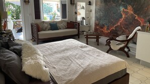 Ein geräumiges Zimmer mit einem großen Bett, einer Couch, einem Esstisch und einem Wandgemälde.