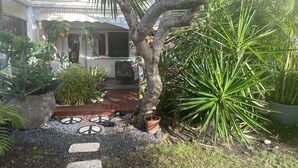 Ein Garten mit verschiedenen Kübelpflanzen, einer Holzterrasse und einem gepflasterten Weg.
