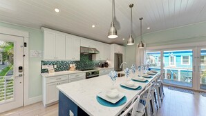 A modern kitchen with white cabinets, a large island, and pendant lighting. - Blue Hideaway- 5 bedroom with Separate Guest House, Private Pool/Spa! (Anna Maria)