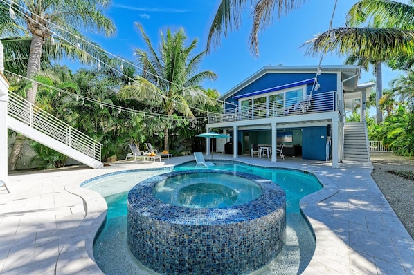 A modern house with a pool, a covered patio, and a staircase leading to a balcony.
